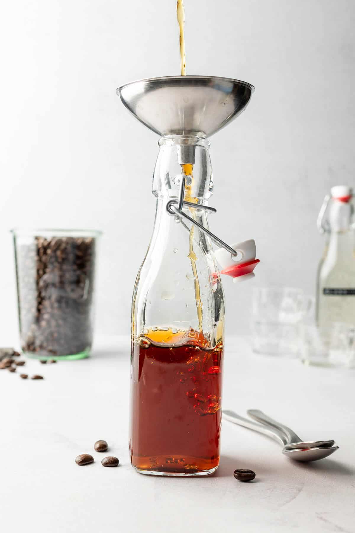 Brown sugar syrup is pouring through metal funnel into swing top glass jar.