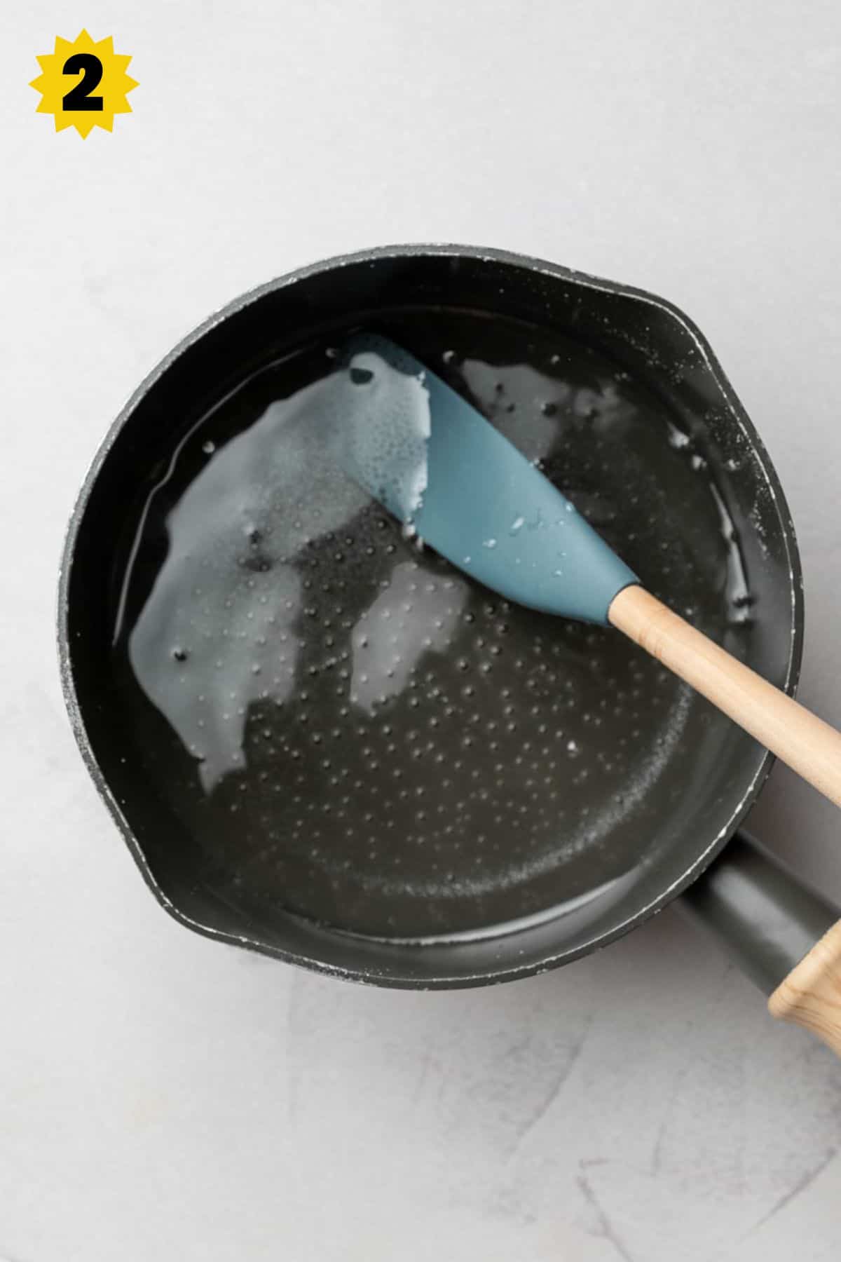 Small saucepan with clear simple syrup and simmering bubbles on the bottom.