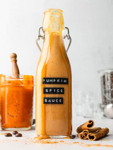 Pumpkin spice sauce drizzling down the side of a tall glass jar.