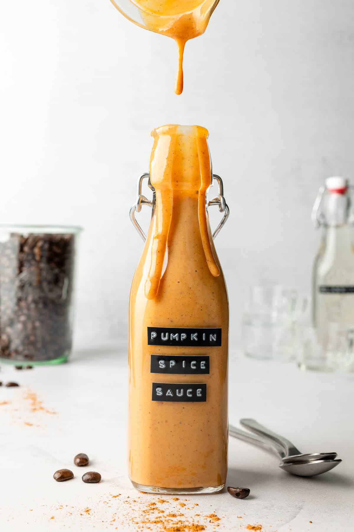 Pumpkin spice sauce pouring into tall glass bottle.