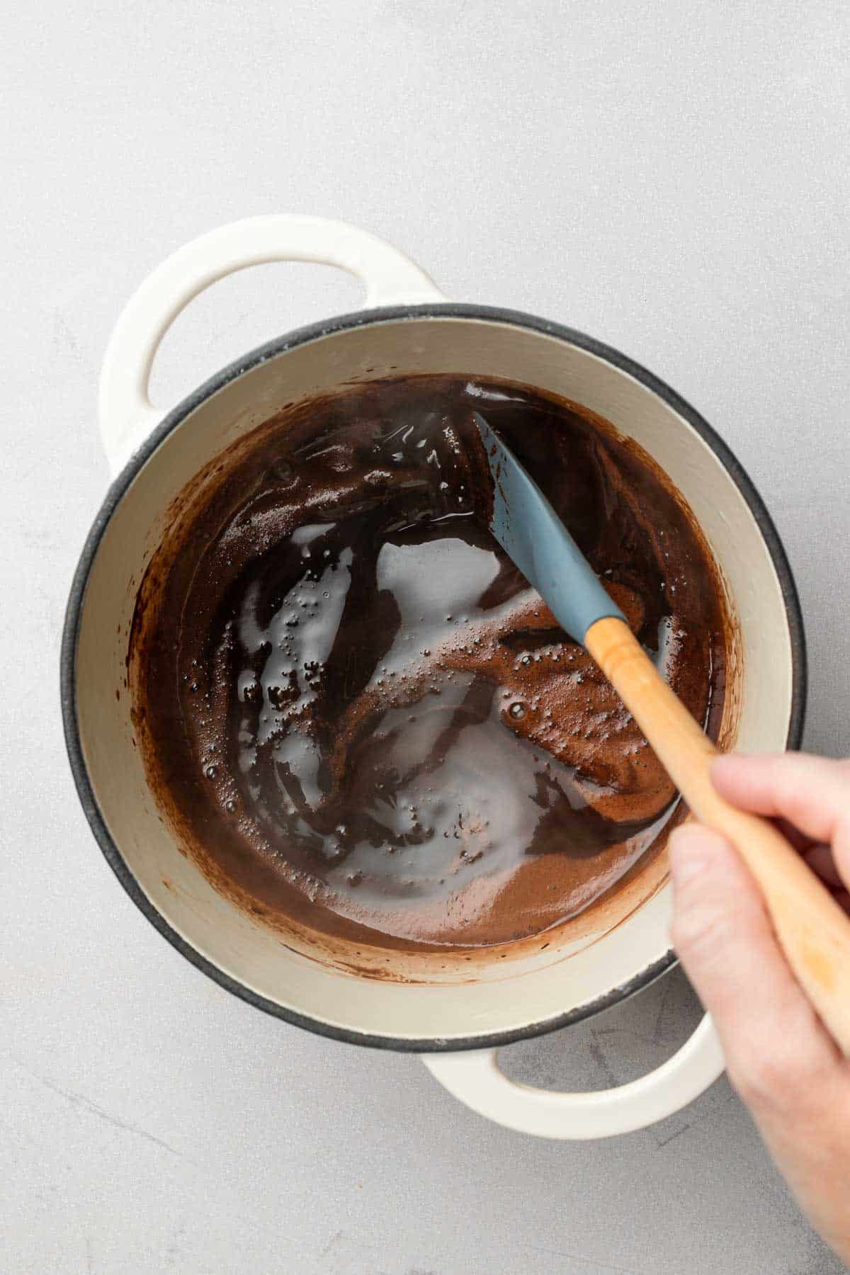 Mocha sauce bubbling in small saucepan, stirred by spatula.