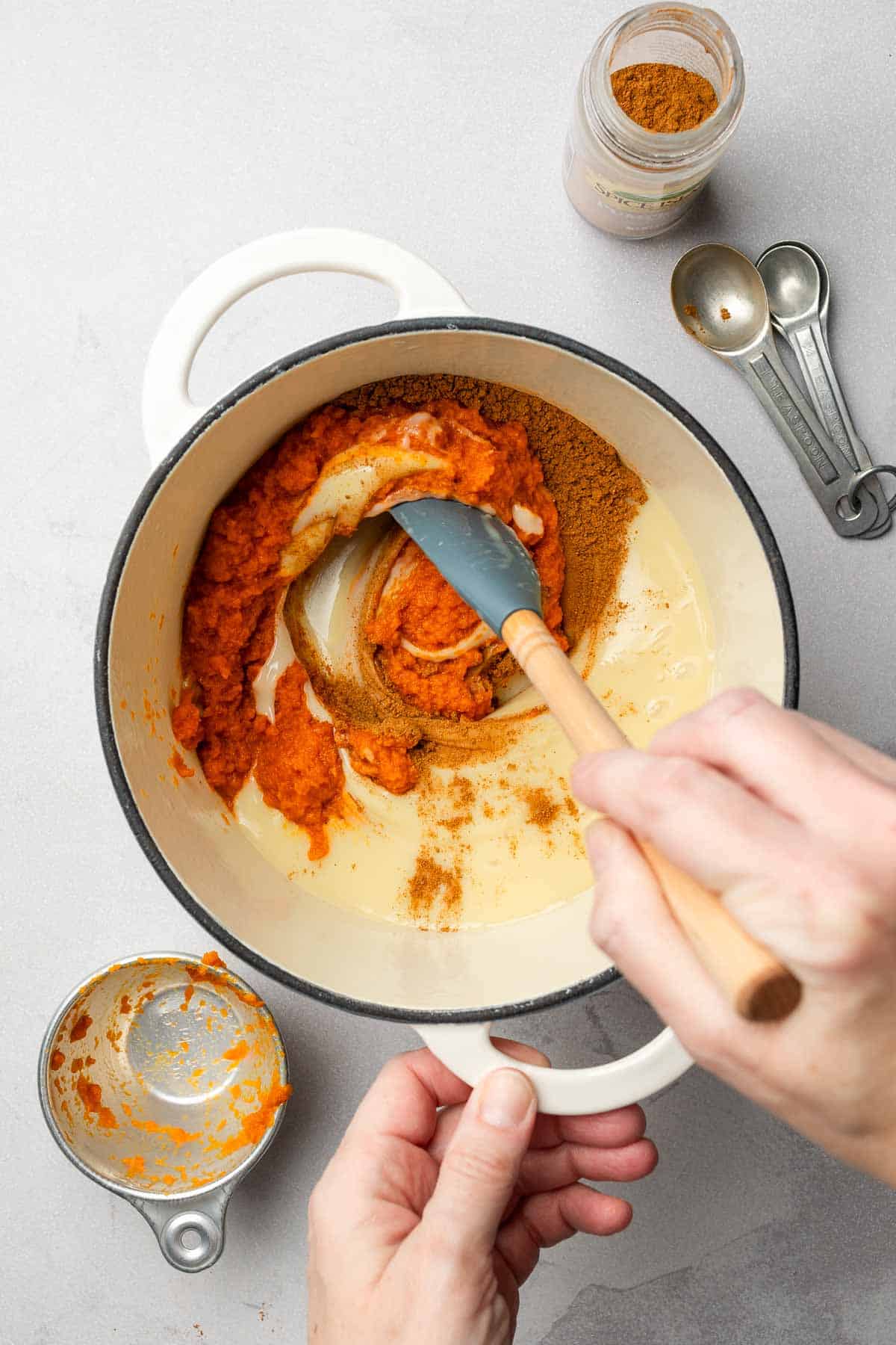 Hand stirring condensed milk, pumpkin, and spices in saucepan.