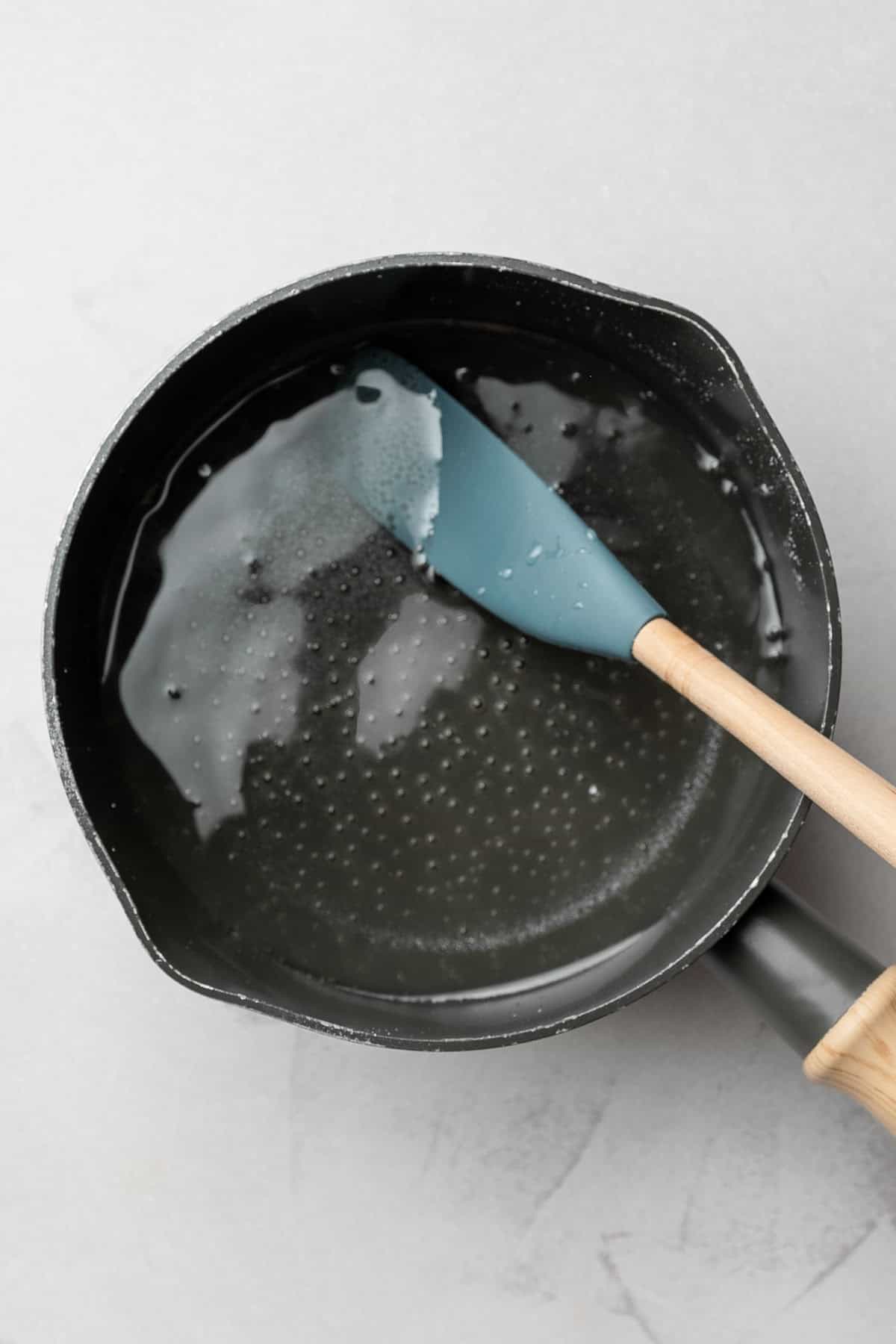 Simple syrup in small sauce pan with simmering bubbles and rubber spatula.