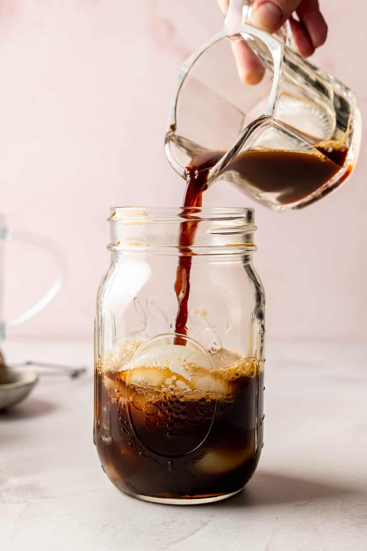 A close-up of dark espresso being poured into a mason jar with ice, creating rich coffee layers.