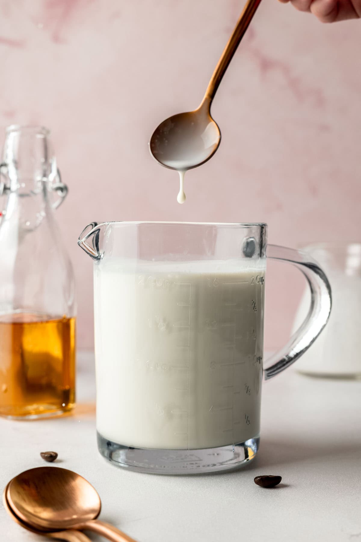 A spoon lifted above the prepared sweet cream mixture, with a drop falling back into the glass measuring cup.