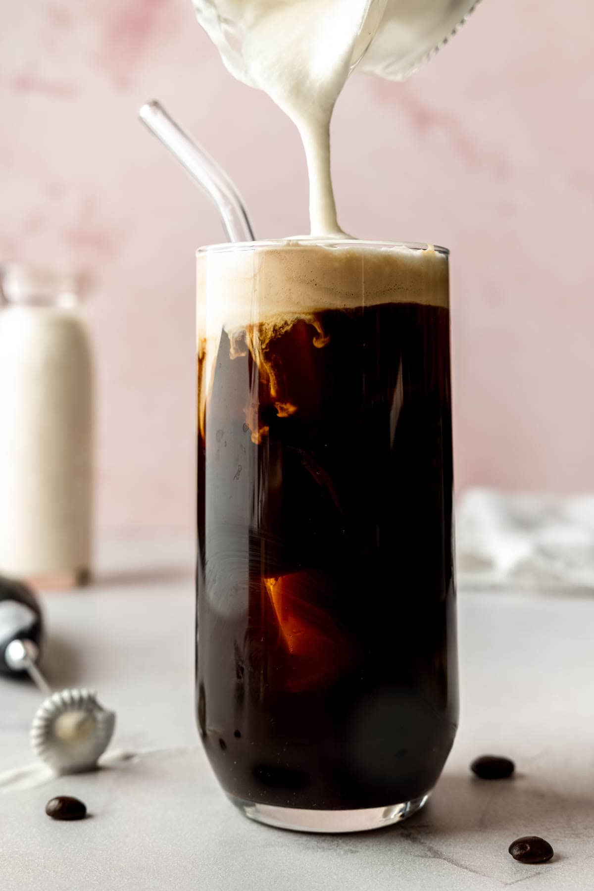 Vanilla sweet cream cold foam being poured over a glass of cold brew coffee, creating creamy swirls.