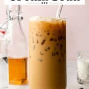 Semi-overhead shot of an iced espresso cream soda with a glass straw, showing creamy bubbles and crushed ice on top. Coffee beans and ingredients are scattered nearby.