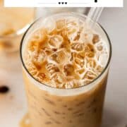 Semi-overhead shot of an iced espresso cream soda with a glass straw, showing creamy bubbles and crushed ice on top. Coffee beans and ingredients are scattered nearby.
