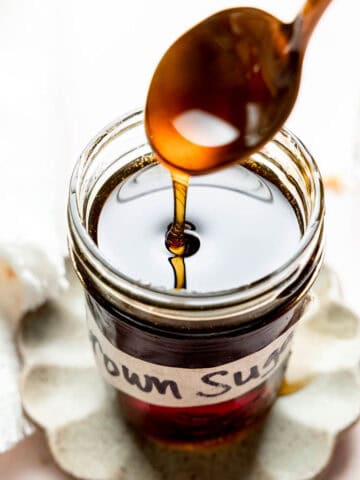 Brown sugar syrup pouring from spoon into a mason jar.