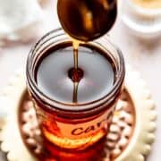 Caramel syrup pouring from spoon into a mason jar.