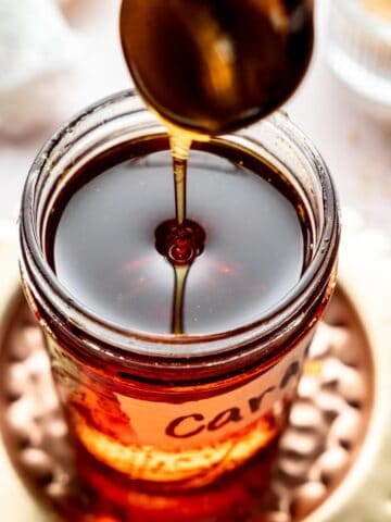 Caramel syrup pouring from spoon into a mason jar.
