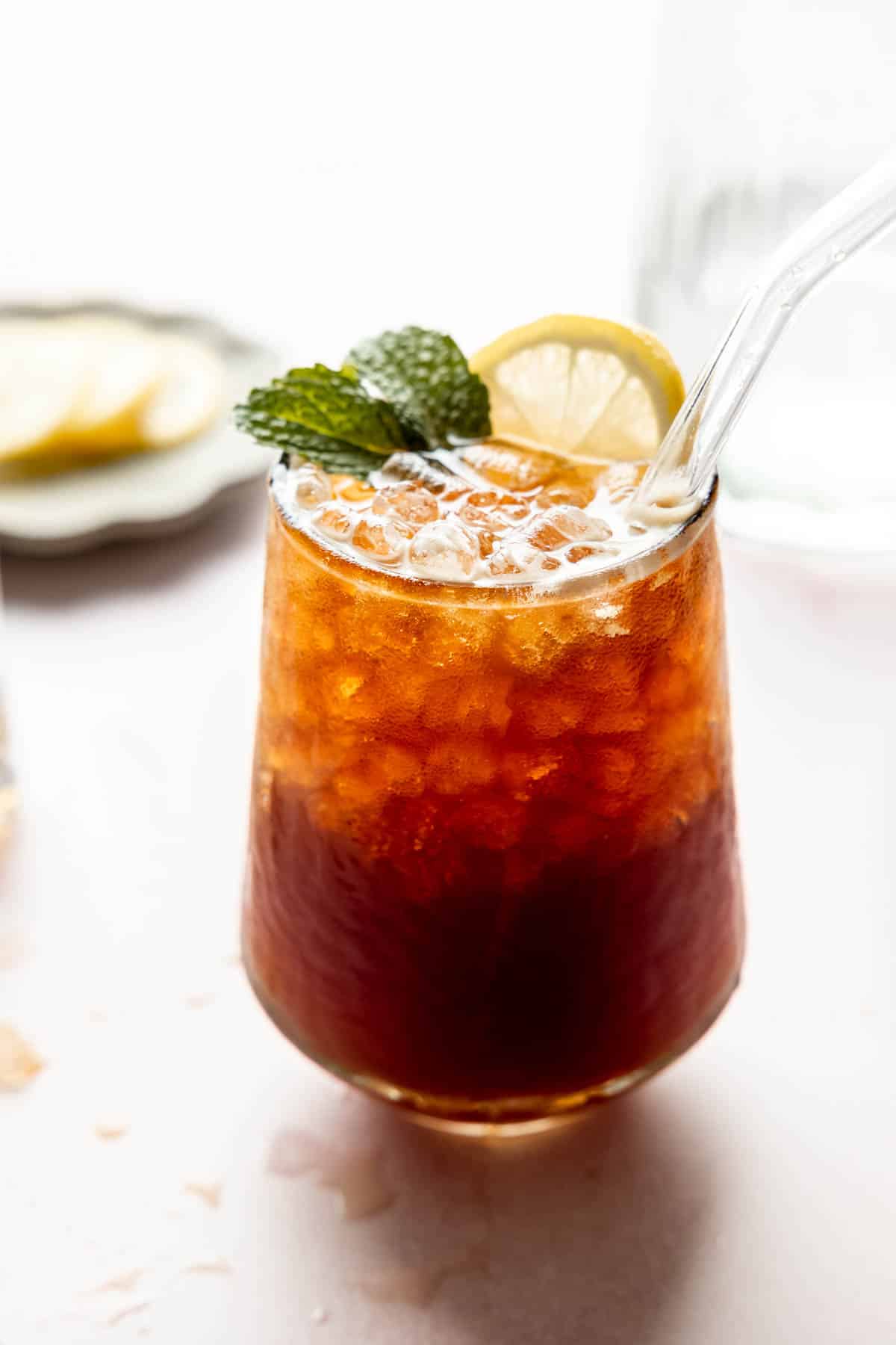A glass of bubbly coffee soda in a stemless wine glass, garnished with a sprig of mint and a slice of lemon.