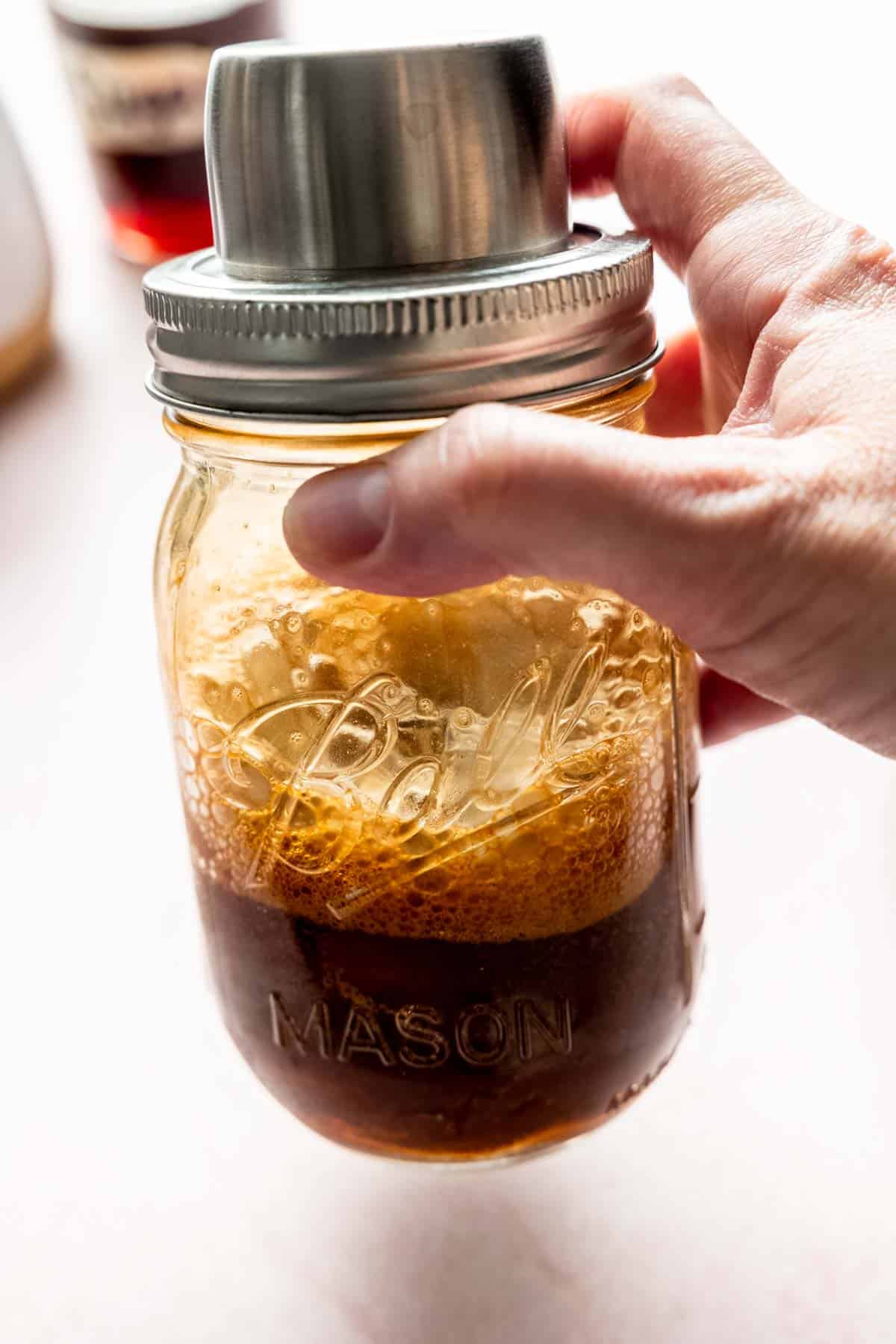 A mason jar with ice and frothy shaken espresso.