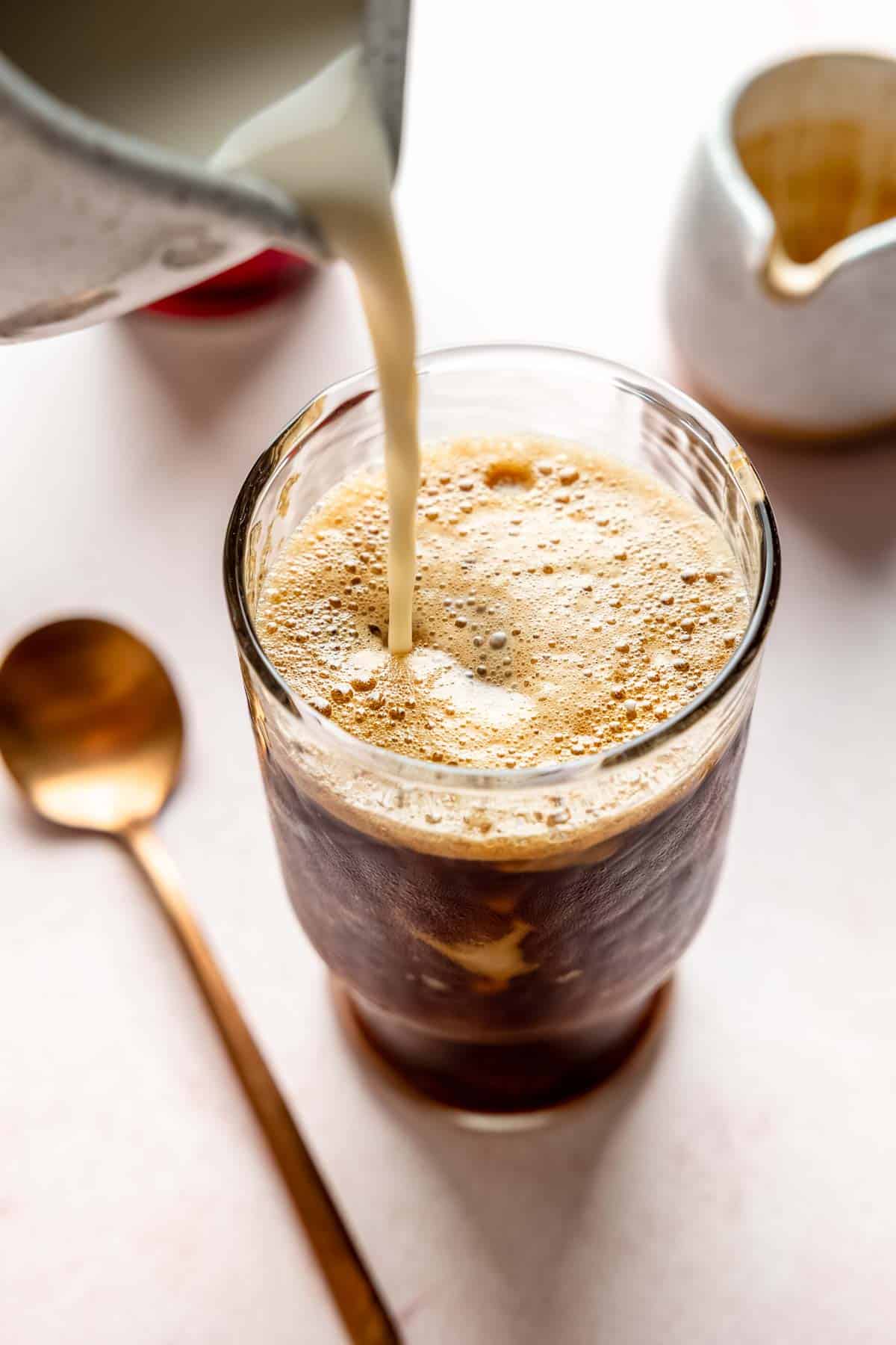 Pouring milk into a tall glass filled with frothy shaken espresso.