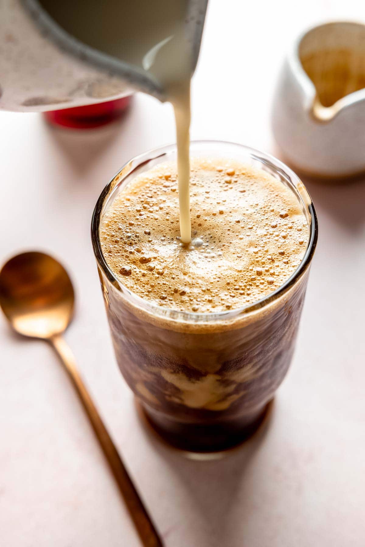 Pouring milk into a tall glass filled with frothy shaken espresso.