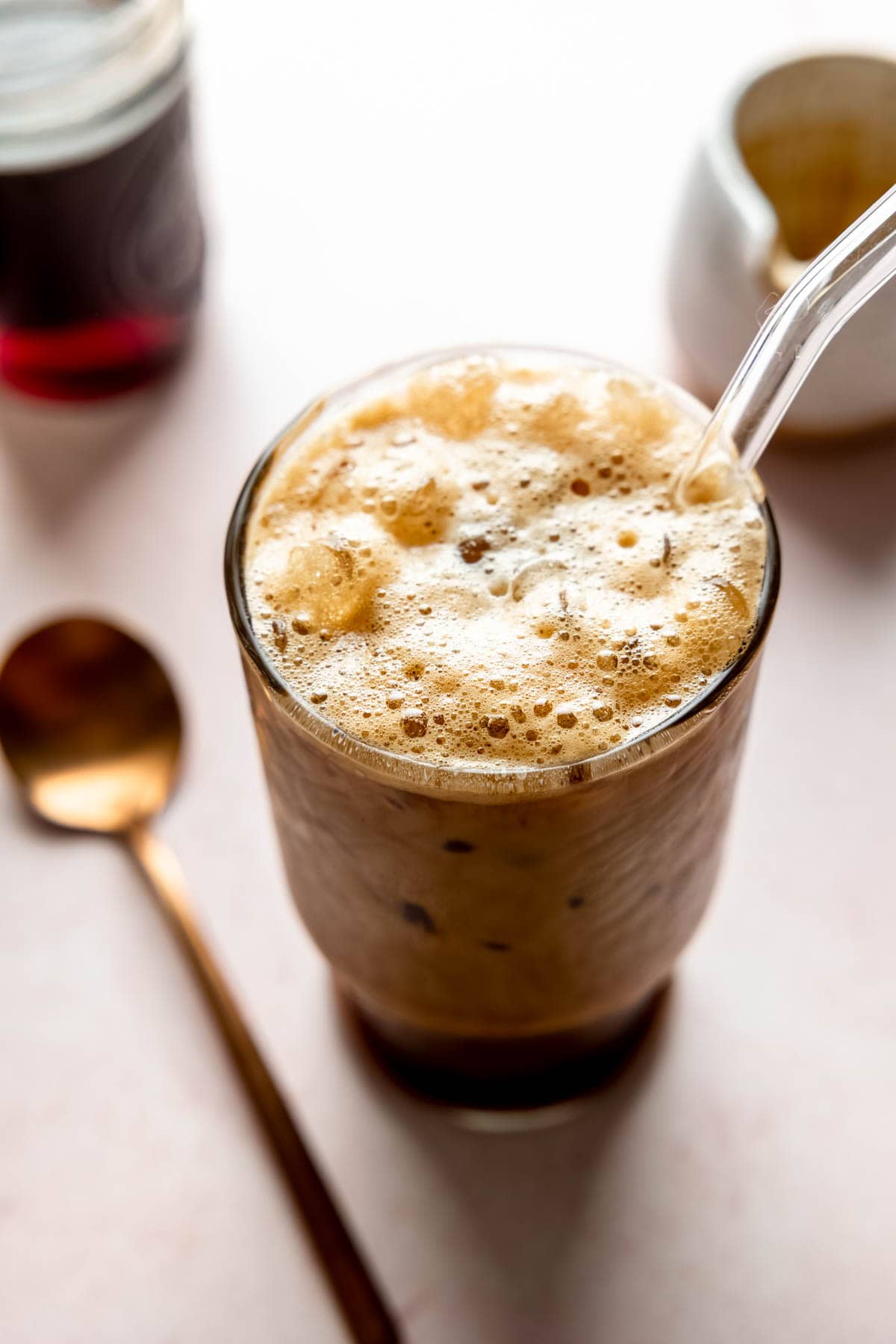 Frothy bubbles on top of a brown sugar shaken espresso in tall glass with glass straw.