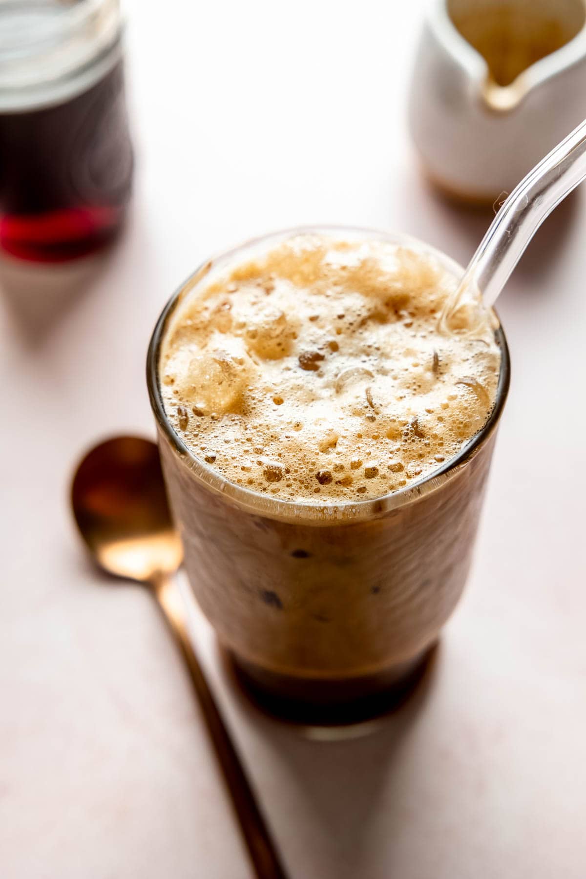 Frothy bubbles on top of a shaken espresso in tall glass with glass straw.