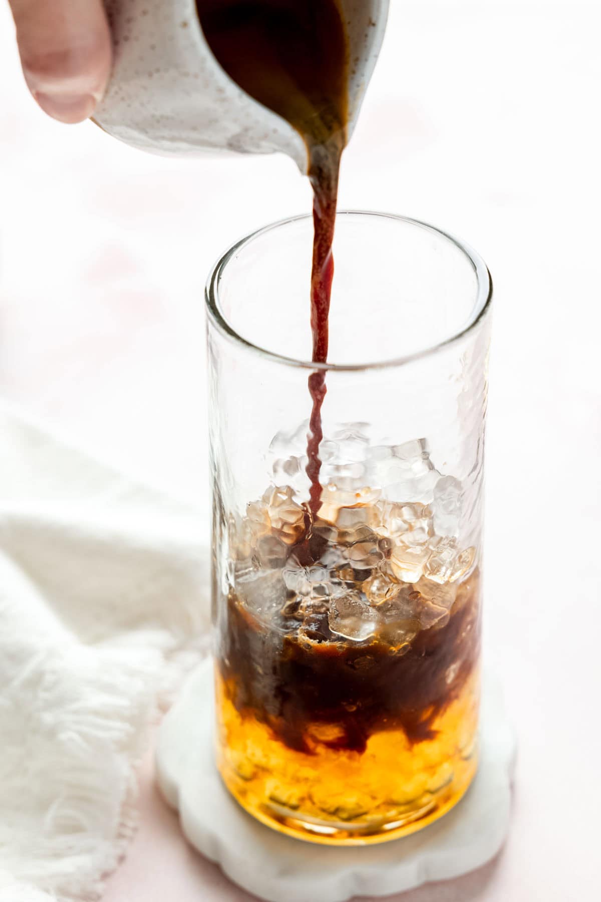 Pouring espresso into tall glass with ice and caramel syrup.