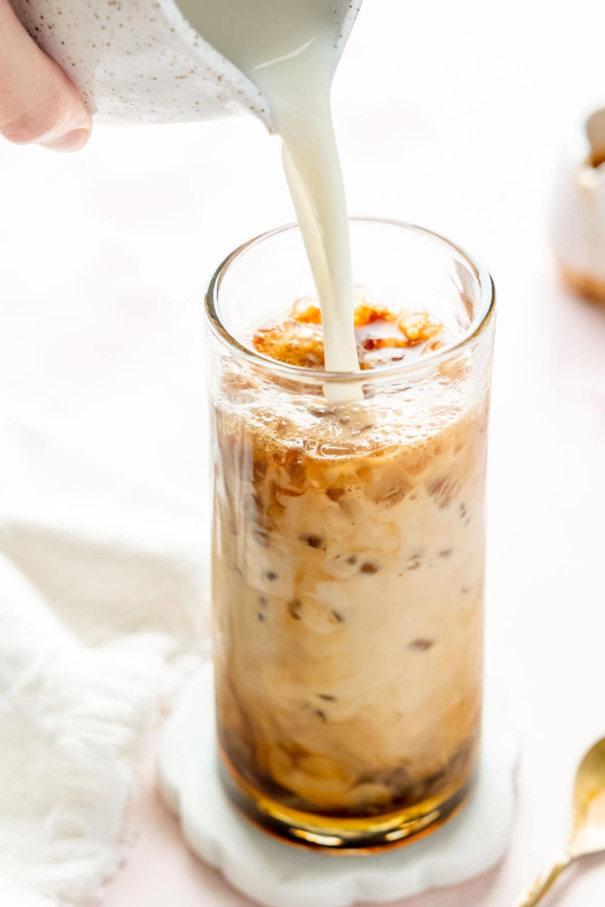 Pouring milk into tall glass filled with ice, espresso, and caramel syrup.