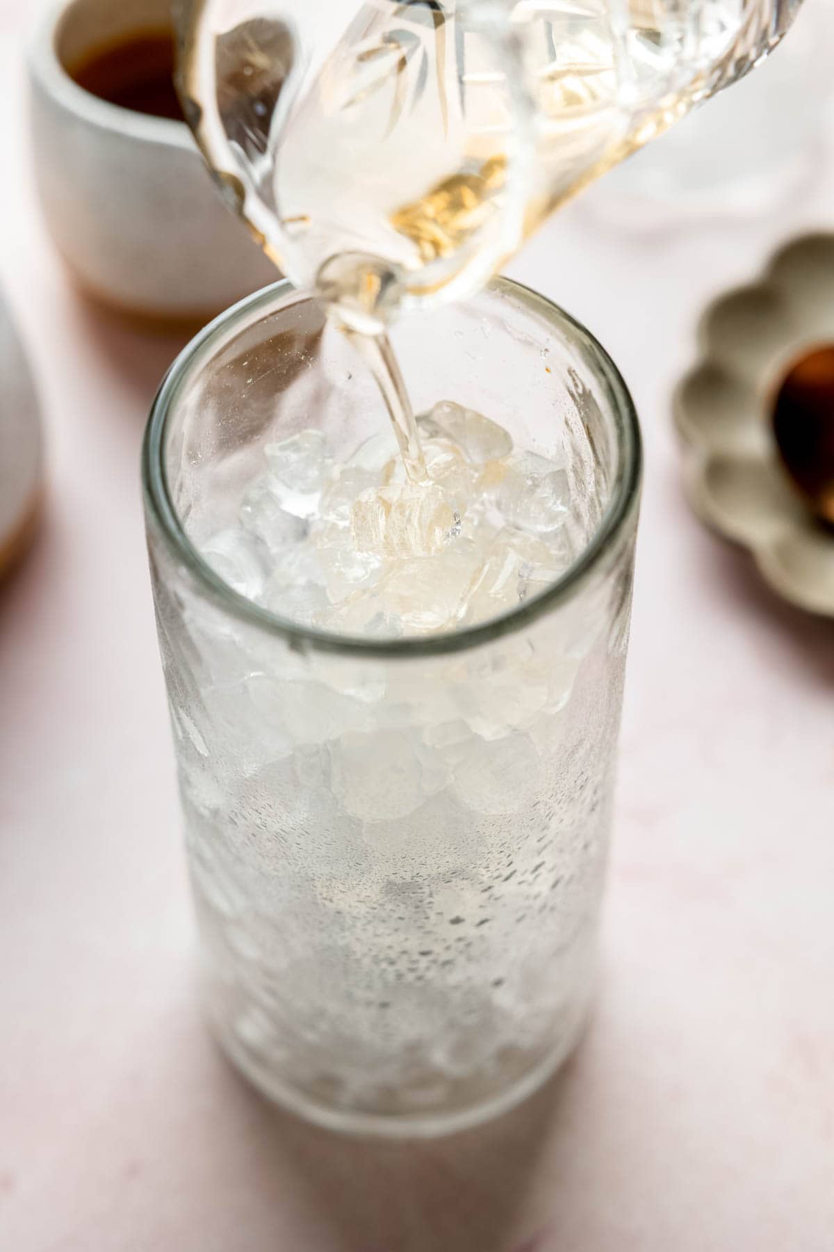 Pouring vanilla syrup into a tall glass filled with ice.