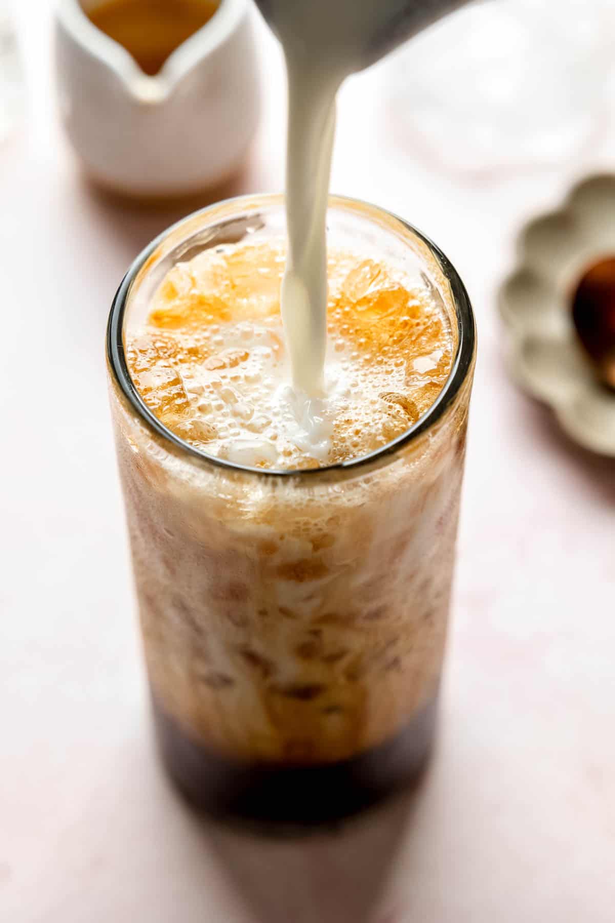 Pouring milk into a tall glass filled with ice and espresso.