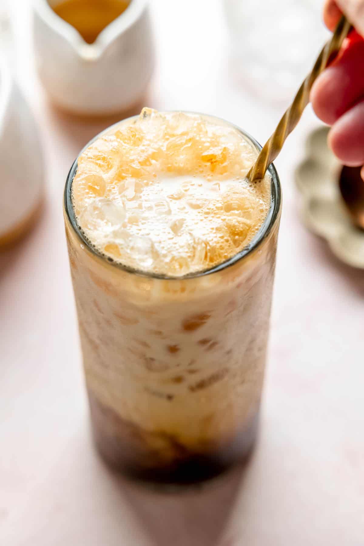 Hand stirring vanilla latte in tall glass.