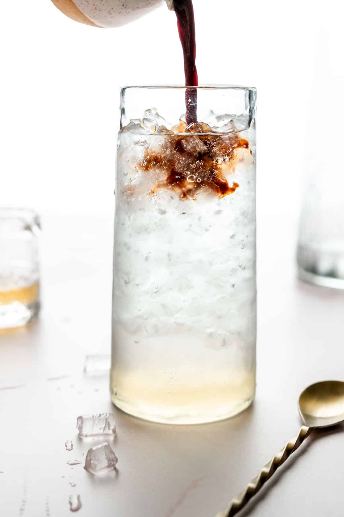 A tall glass filled with ice, vanilla syrup, and seltzer water; espresso poured on top.