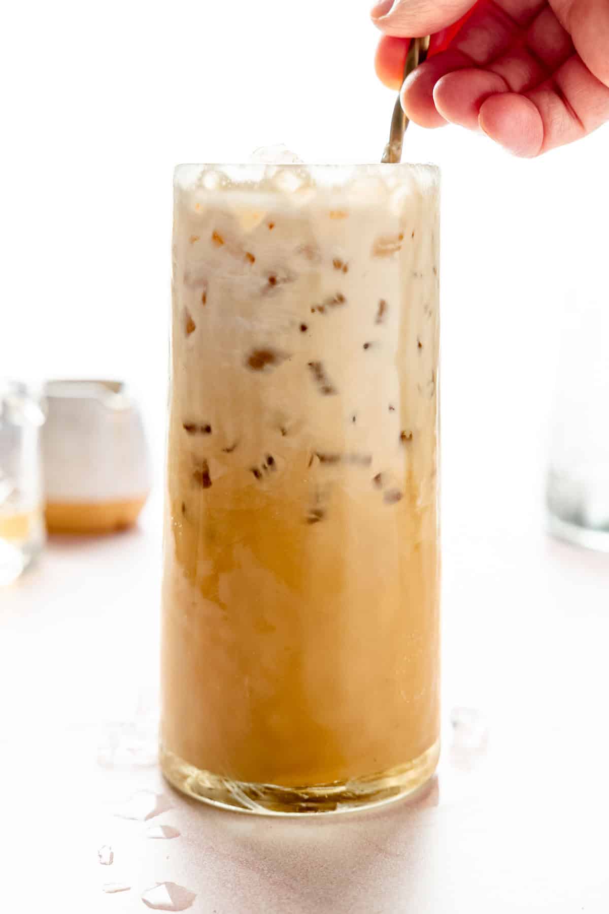 A hand stirring the creamy and espresso layers of the drink together.