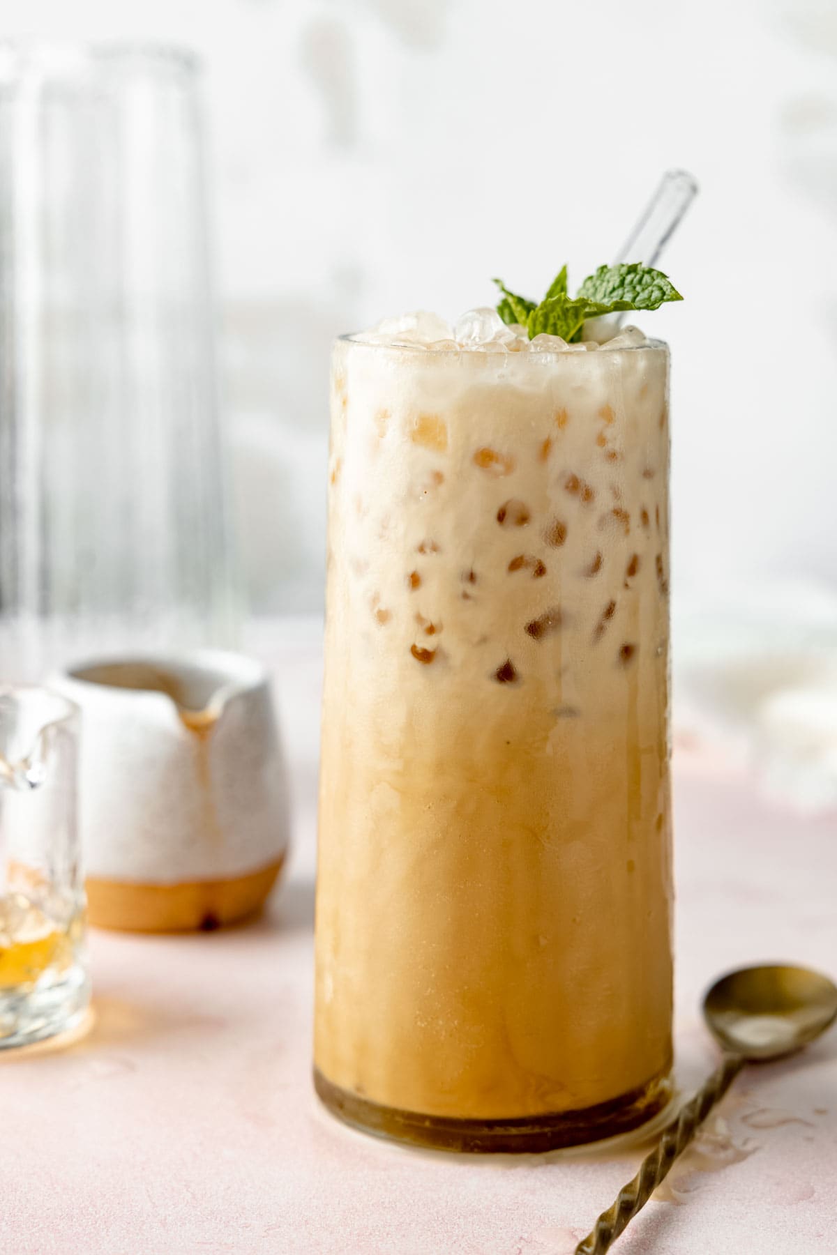 A sprig of mint garnishes a tall glass filled with a creamy coffee drink and nugget ice.