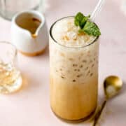 Semi-overhead shot of an iced espresso cream soda with a glass straw, showing creamy bubbles and crushed ice on top, garnished with mint.