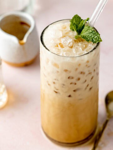 Semi-overhead shot of an iced espresso cream soda with a glass straw, showing creamy bubbles and crushed ice on top, garnished with mint.