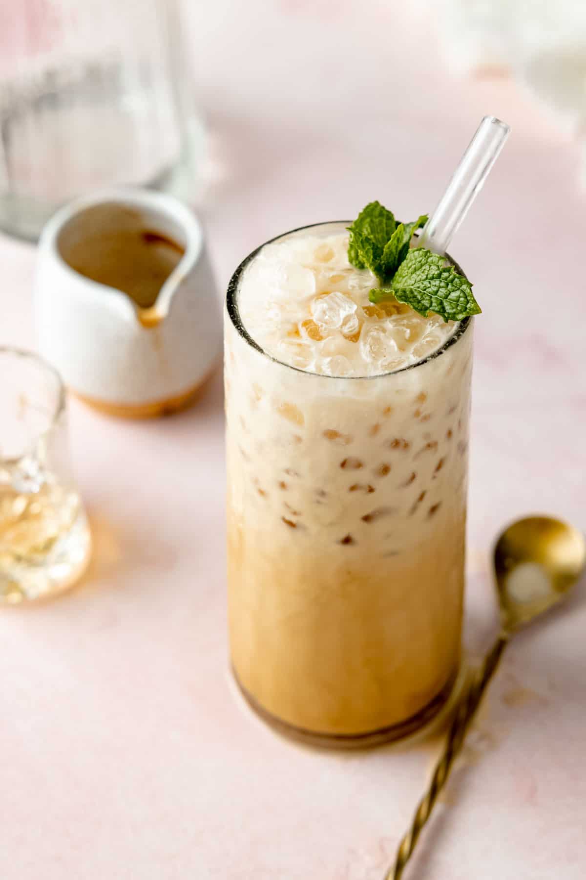 Semi-overhead shot of an iced espresso cream soda with a glass straw, showing creamy bubbles and crushed ice on top, garnished with mint.