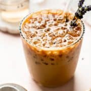 Angled view of iced lavender latte with visible lavender sprigs and a glass straw.
