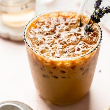 Angled view of iced lavender latte with visible lavender sprigs and a glass straw.