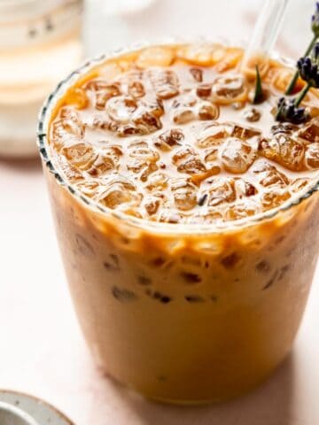 Angled view of iced lavender latte with visible lavender sprigs and a glass straw.