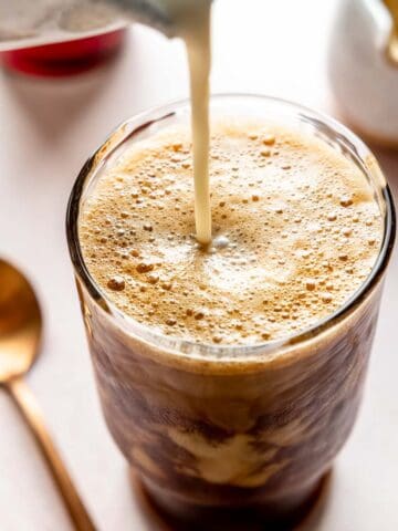Pouring milk into a tall glass filled with frothy shaken espresso.