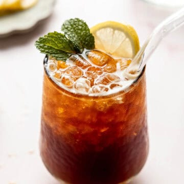 A glass filled with bubble iced coffee soda garnished with a sprig of mint and a lemon slice.