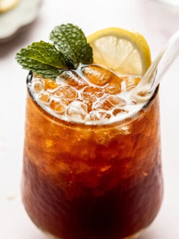 A glass filled with bubble iced coffee soda garnished with a sprig of mint and a lemon slice.