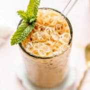 Iced vanilla latte with mint leaves, nuggets of ice, and a glass straw.