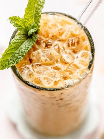 Iced vanilla latte with mint leaves, nuggets of ice, and a glass straw.