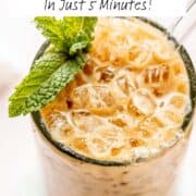 Iced coffee in a tall glass with mint leaves and a spoon.