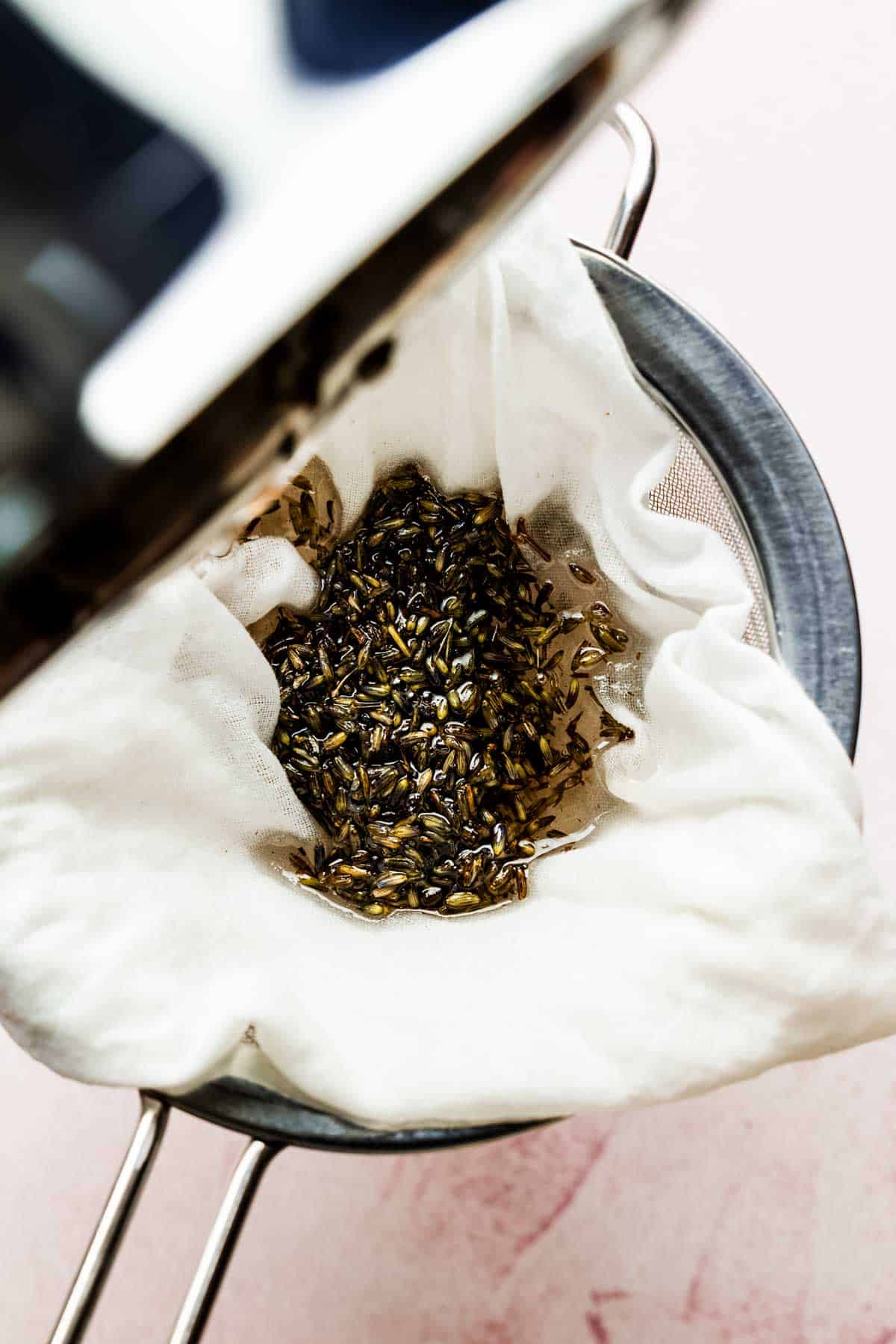 Straining out the lavender buds from the syrup through a fine mesh sieve.