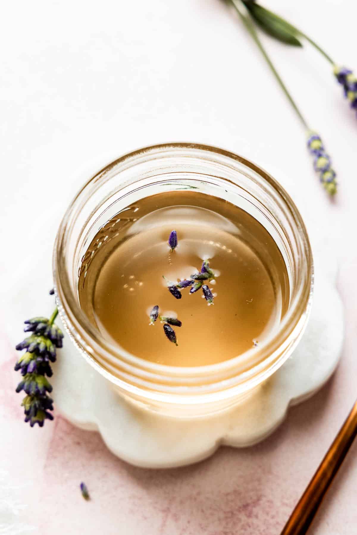 Lavender syrup with golden color in mason jar with lavender buds on top.
