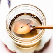 Overhead view of spoon in small mason jar with lavender syrup and lavender buds floating on top.