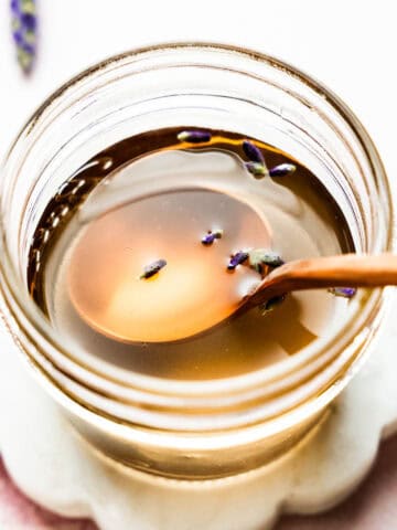 Overhead view of spoon in small mason jar with lavender syrup and lavender buds floating on top.