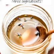 Overhead view of spoon in small mason jar with lavender syrup and lavender buds floating on top.