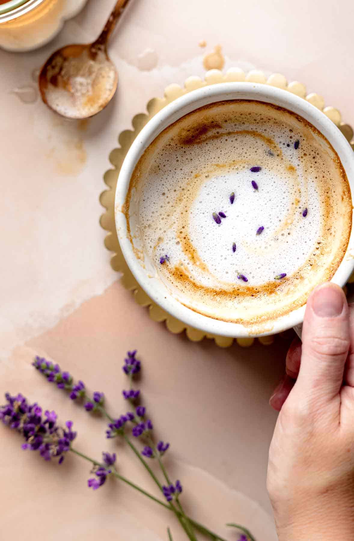 A mug of lavender latte partially drunk, showing frothy milk with lavender buds floating on top.