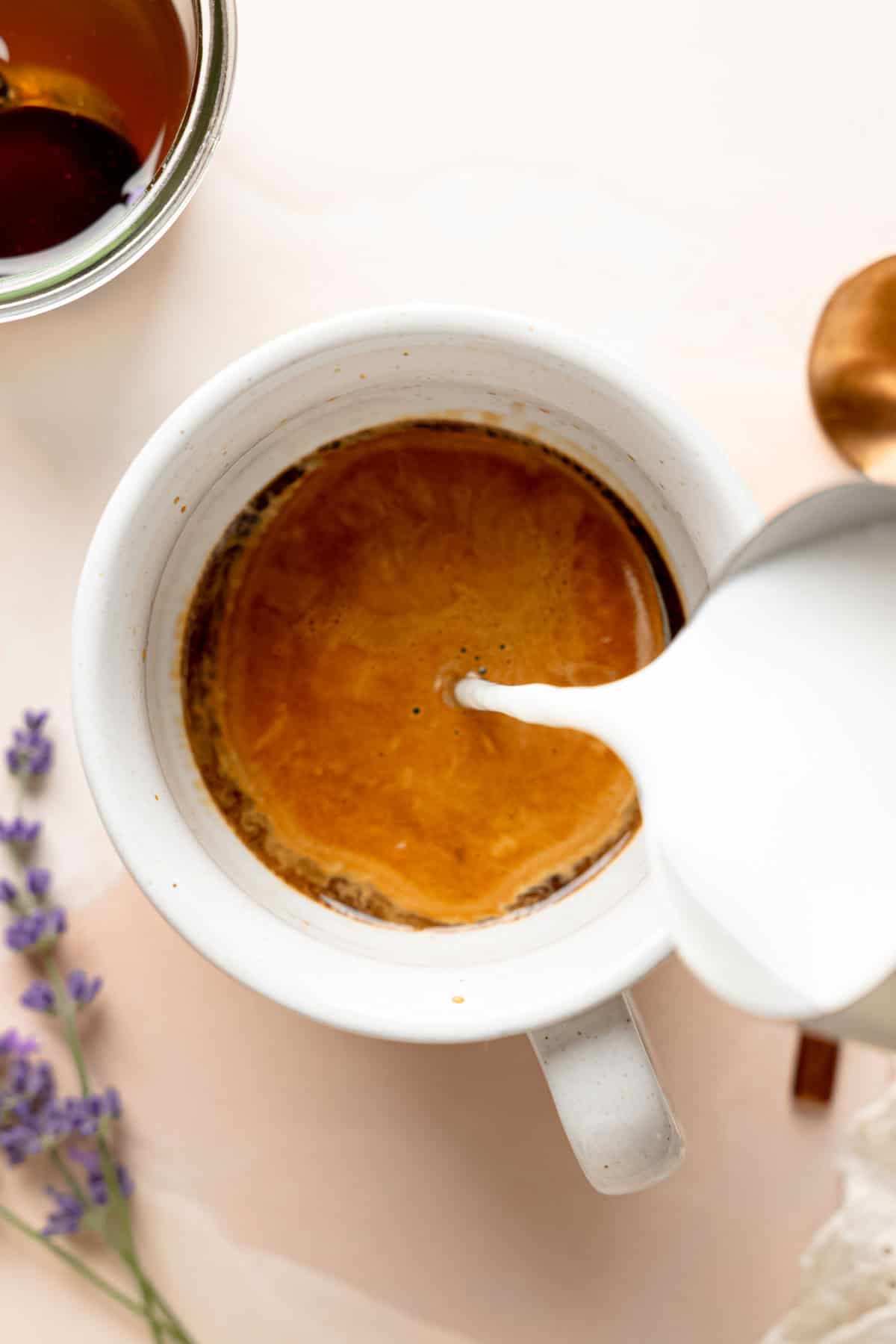 Pouring steamed milk over espresso in cup.