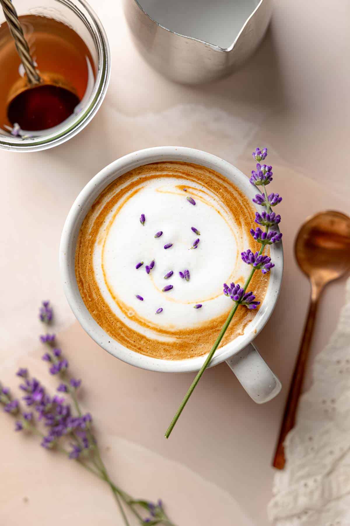 A lavender latte in a mug with foam, lavender buds, and a sprig of fresh lavender resting on top.
