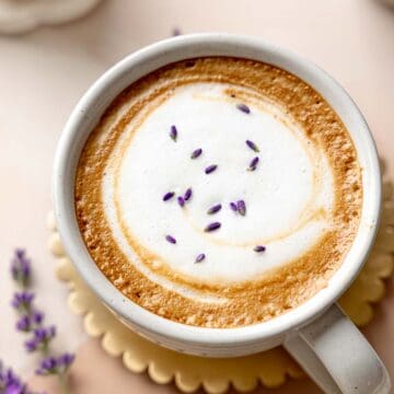 A lavender latte topped with foamy milk and sprinkled with dried lavender buds.